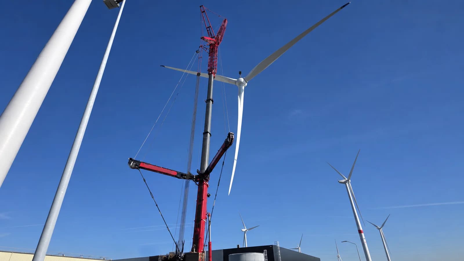 Privacybewerkte praktijkfoto: een mobiele kraan hijst een rotorblad naar een windturbine.